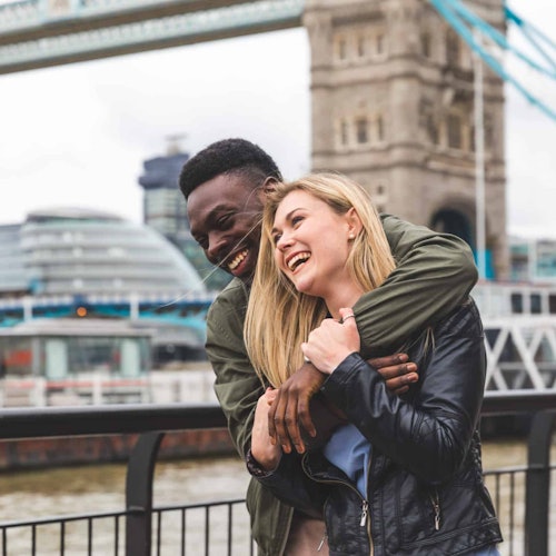 A happy multiracial couple having fun together at the Tower Bridge, one of the most fun things to do in London this summer. 